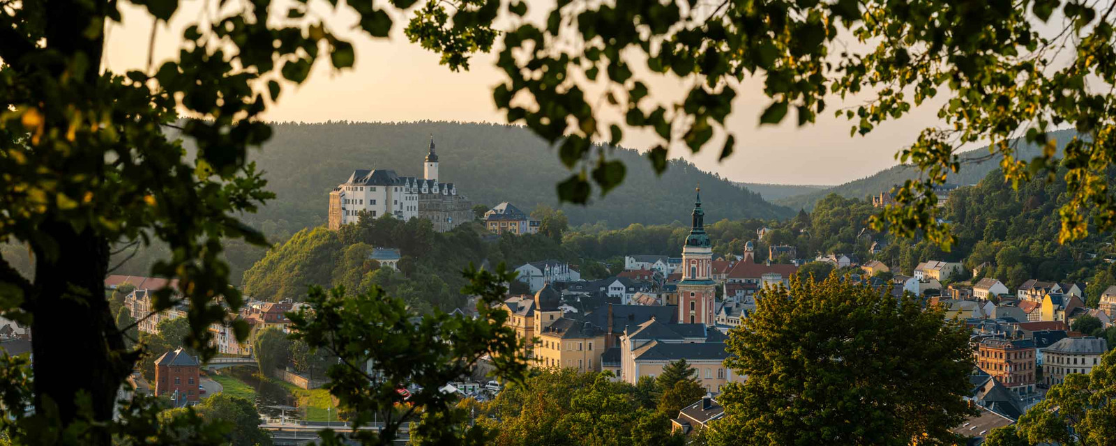Panoramafoto vom oberen Schloss Greiz mit Stadtblick zum Sonnenuntergang umgeben von Blättern