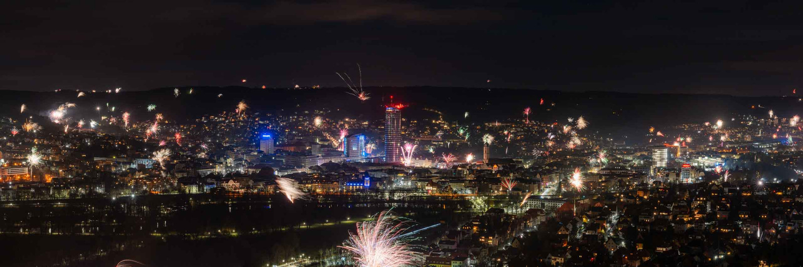 Panoramafoto von Jena zu Silvester mit Feuerwerk und Raketen über der Stadt