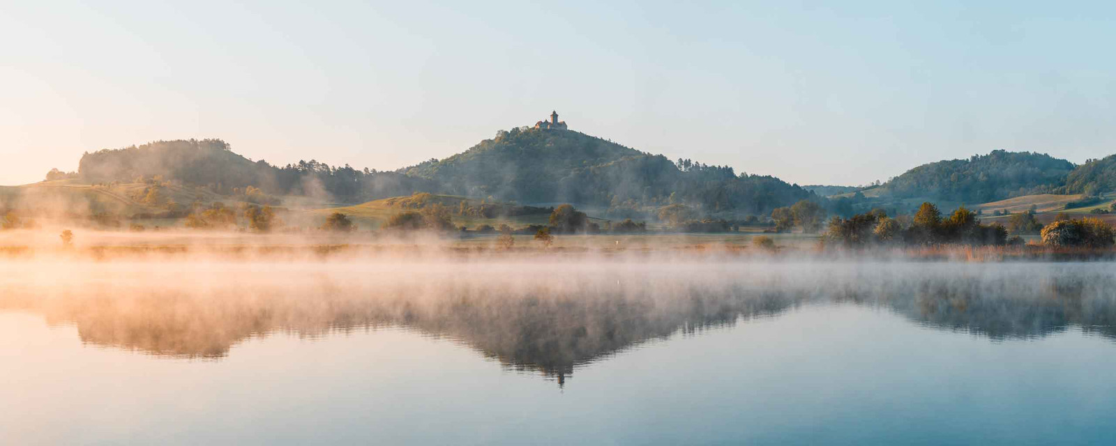 Episches Panorama Foto von der Wachsenburg zum Sonnenaufgang über einem See mit Nebelwolken
